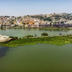 Widok na jezioro i wzgórza Antananarywy, gdzie żyje madagaskar ludność. Widać pomnik, stadion i kwitnące drzewa.