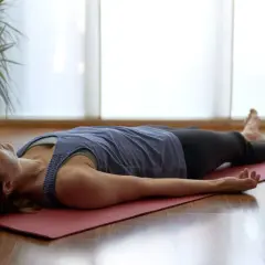Kobieta leży na macie w pozycji Savasana, praktykując jogę nidrę. Jej ciało jest rozluźnione, a dłonie skierowane ku górze.