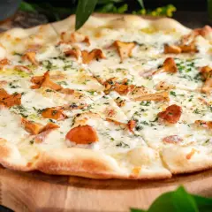 Pyszna pizza z kurkami, rozpływającym się serem i ziołami, podana na drewnianej desce.