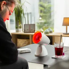 Mann mit rotlicht bei fieber, der sich auf eine Wärmelampe konzentriert. Daneben ein Glas mit rotem Getränk.