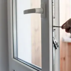 Main tenant utilise un tournevis pour régler une porte fenêtre 2 vantaux.