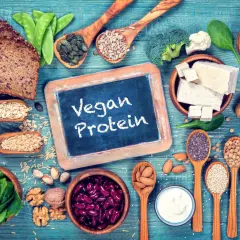 Na stole pełnym roślinnych produktów: chleb, fasola, orzechy, nasiona, tofu, warzywa i jogurt. To dowód, że wegańskie białko jest łatwo dostępne i smaczne.