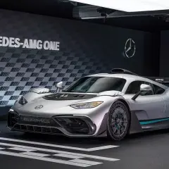 Srebrny Mercedes-AMG ONE, hiperauto z elementami wyścigowymi, prezentuje się na tle ściany z logo i napisem "MERCEDES-AMG ONE".