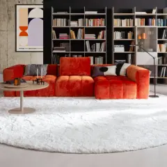 Ein flauschiger weißer Teppich bildet die Basis für das orangefarbene Sofa. So lässt sich der Teppich unter dem Sofa richtig platzieren.
