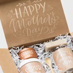 Otwarty brązowy karton z napisem "Happy Mother's Day" i zawartością: świeca, peeling, mydło, kubek i drewniana łyżeczka.