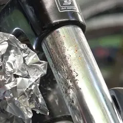 Mano che strofina con carta stagnola un ammortizzatore di bicicletta con macchie di ruggine e sporco.
