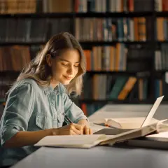 Młoda kobieta w bibliotece pisze notatki, inspirując się książkami motywacyjnymi top 10.