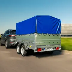 Przyczepa kempingowa bez prawa rejestracji, z niebieską plandeką, ciągnięta przez ciemny SUV.