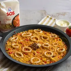 Fideuá con calamares lista para servir, acompañada de tomates y alioli.
