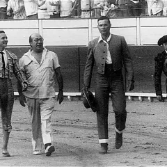 Un sayalero y un bandrés caminan juntos en la arena. El sayalero, con traje de luces, saluda.