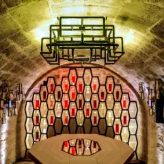 Ambiance unique aux Caves du Louvre, avis sur ce lieu historique et moderne. Bouteilles illuminées dans des alvéoles, table centrale.