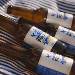 Butelki piwa bezalkoholowego POLAN leżą na kocu w paski. Czy piwo bezalkoholowe ma alkohol? Nie, to napój dla każdego.