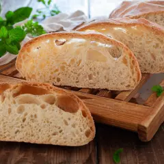 Fette di pane soffice con alveolatura pronunciata, su un tagliere di legno, con foglie di menta fresca.