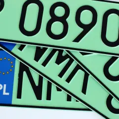 Kilka zielonych tablic rejestracyjnych z czarnymi numerami i literami, jedna z nich ma niebieski pasek z gwiazdkami UE i napisem PL.