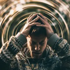 Mężczyzna z rękami na głowie, otoczony wirującymi liniami, symbolizującymi psychosomatykę i wewnętrzny niepokój.