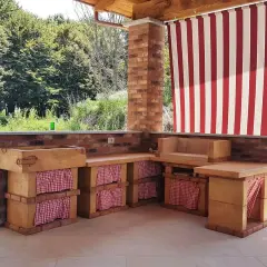 Cucina esterna in muratura fai da te con lavello, piano di lavoro e seduta. Tende a righe rosse e bianche proteggono lo spazio.