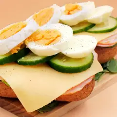 Pyszna kanapka z jajkiem, plastrami ogórka, serem i szynką, doprawiona pieprzem. Idealna na śniadanie.