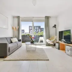 Jasne, nowoczesne mieszkanie bezczynszowe z szarą kanapą, dywanem, stolikiem kawowym i telewizorem.