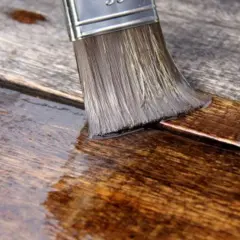 Pennello stende olio paglierino per legno su assi grezze, nutrendo e proteggendo la superficie.
