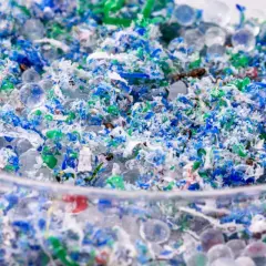 Kolorowe fragmenty plastiku i przezroczyste kuleczki, przypominające mikrokoraliki, tworzą obraz zanieczyszczenia. To mikroplastik w wodzie, widoczny w szklanym naczyniu.
