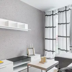 Nowoczesny salon z szarą ścianą pokrytą tynkiem japońskim o subtelnych wzorach. Białe meble i zasłony w kratę.