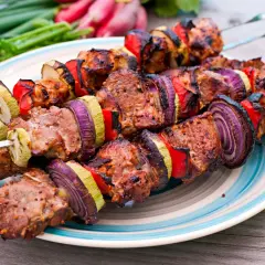 Brochettes d'agneau grillées avec oignons rouges, poivrons et courgettes sur une assiette, prêtes à être dégustées.