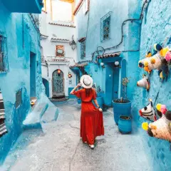 Una mujer con vestido rojo pasea por una calle de la **marruecos ciudad azul**, decorada con coloridas artesanías.
