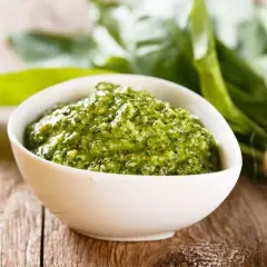 Pesto verde in una ciotola bianca, con un fascio di foglie di sedano fresche sullo sfondo. Perfetto per le tue ricette.