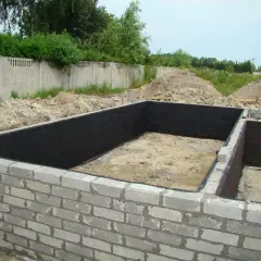 Fundament z bloczków betonowych, wewnątrz czarna izolacja. Widać kilka warstw bloczka fundamentowego.