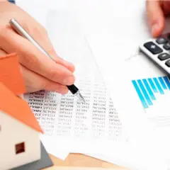 Man calculando el precio tasación vivienda con calculadora y modelo de casa.