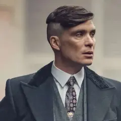 En sidbena kille med en distinkt frisyr och en elegant kostym.