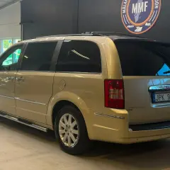 En gyllene Chrysler Voyager står parkerad. Den har en takbox och en svensk registreringsskylt.