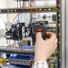 Ręka reguluje panel sterowania w szafie elektrycznej. Zastanawiasz się, ile zarabia magister inżynier elektryk?