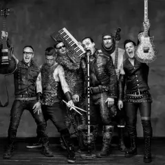 Zespół Rammstein, w tym Till Lindemann, gotowy do rockowego występu. W tle klawisze i gitary, jak w ich hicie "Radio".