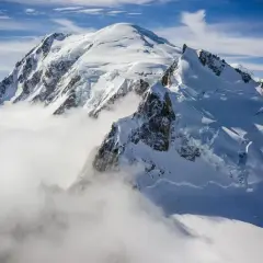 Le Mont Blanc, majestueux et enneigé, émerge des nuages. Des alpinistes escaladent ses pentes glacées sous un ciel bleu éclatant.