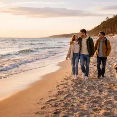 Trzech przyjaciół i pies spacerują po piaszczystej plaży w Mielnie o zachodzie słońca.