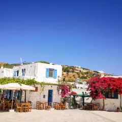 Un angolo di **Grecia con bambini** che giocano felici tra i tavolini di un caffè, sotto bouganville fiorite e il cielo azzurro.