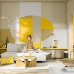 Eine Frau entspannt sich in einem hellen Wohnzimmer mit geometrischer Wandgestaltung. Welche Farbe passt zu Gelb? Hier: Beige, Grau und Weiß harmonieren perfekt.