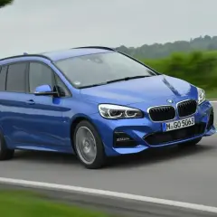 Niebieskie BMW 218i w wersji kombi pędzi po drodze, otoczone zielenią i drzewami.