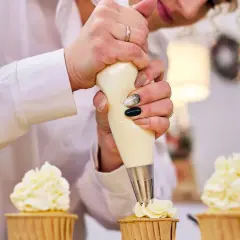Une pâtissière décore des cupcakes avec une chantilly mascarpone aérienne.