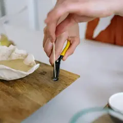 Ręce z narzędziem mocują knot do świeczki. To prosty sposób, jak zrobić knot do świeczki.