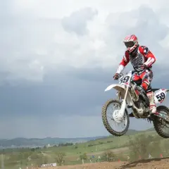 Motocrossowiec w skoku na motocyklu, podobnym do Husqvarna Motorcycles i KTM, w czerwono-białym stroju.
