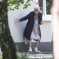 Beata Tyszkiewicz w domu opieki, z kubkiem w dłoni, oparta o ścianę.