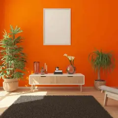 Arredamento moderno con pareti arancioni vivaci. Un tavolino bianco con piante verdi e decorazioni, un quadro vuoto e una poltrona grigia.