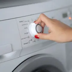 Main d'une femme sélectionnant le programme synthétique sur une machine à laver.
