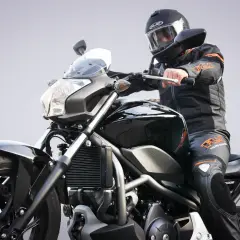 Motocykl od ilu lat? Młody motocyklista w czarnym kombinezonie i kasku na czarnym motocyklu.
