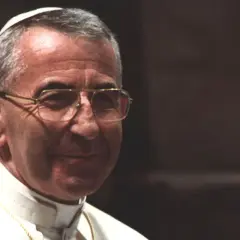 Porträt von Papst Johannes Paul I. mit Brille und Soutane, im Hintergrund eine goldene Statue.