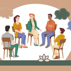 Grupa ludzi na sesji, gdzie terapeuta wyjaśnia, socjoterapia co to jest. Dyskutują w kręgu, dzieląc się myślami.