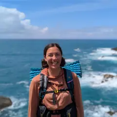 A smiling hiker with a backpack and sleeping pad enjoys the view of the ocean waves crashing on the shore along the Fischerweg trail in Portugal.