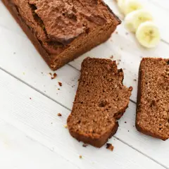 Chlebek bananowy Ani gotuje się na białych deskach. Obok leżą dwa kawałki ciasta i plasterki banana.
